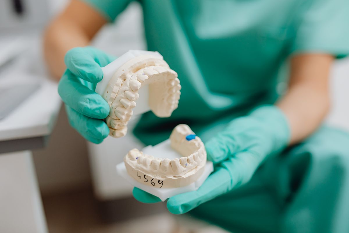 Stomatolog prezentuje pacjentowi model implantów i mostu protetycznego